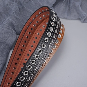 Close-up of metal eyelet belt with white stitching and punk style silver hardware detail
