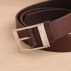 Macro shot of dark brown leather belt with minimalist silver rectangle pin buckle on wood