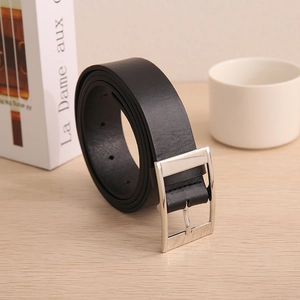 Detail of a black leather belt with silver rectangular buckle on a light wood surface