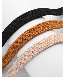 Dettaglio di tre cinture intrecciate elastiche in nero, marrone e beige con trama a spina
