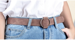 Close-up of brown suede leather belt with silver circular buckle on blue jeans