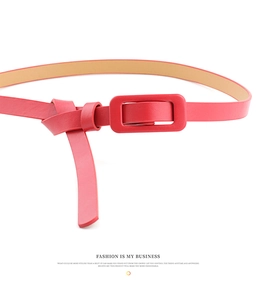 Detail shot of a slim red patent leather belt with a matching color square buckle and smooth finish