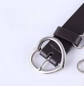 Detail view of a silver heart-shaped buckle on a dark brown leather belt for women