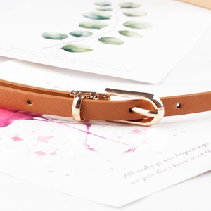 Sottile cintura in pelle marrone per abiti con fibbia a D dorata su sfondo minimalista