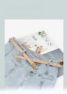 Détail d'une ceinture fine en cuir beige avec boucle dorée sur un jean bleu clair