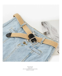 Close-up of beige woven elastic belt with silver square buckle on blue denim jeans