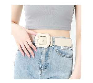 Detail of cream leather belt with wavy square buckle styled on light blue denim jeans