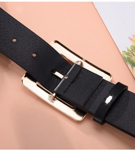 Detail of black pebbled leather belt with a large polished gold rectangular buckle