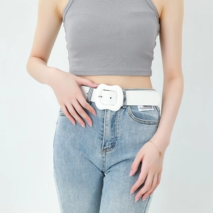 White faux leather belt for women featuring a large wavy buckle worn with casual denim jeans