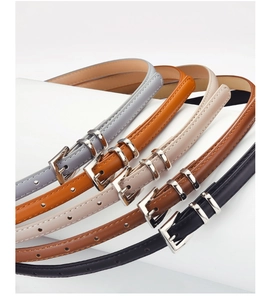 Detail view of five assorted slim leather belts with silver metal buckles on white pedestals
