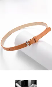 Détail d'une fine ceinture en cuir caramel avec boucle argentée polie sur support blanc