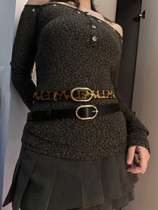 Detail of leopard print and black leather belts with gold oval buckles on a model