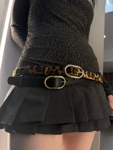 Detail of leopard print and black leather belts with golden oval buckles on model waist