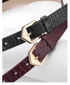 Dettaglio macro di cinture in pelle PU bordeaux e nera con stampa coccodrillo e fibbia in lega