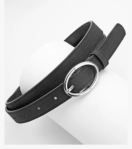 Detail of minimalist black suede thin belt featuring a silver oval buckle on white stand