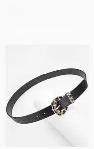 Detail of black faux leather belt featuring an ornate gold buckle with floral engravings