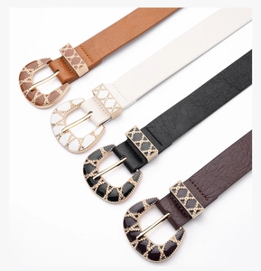 Close-up of four skinny faux leather belts featuring vintage engraved gold buckles in various colors