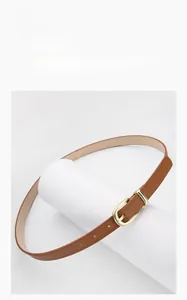 Détail d'une ceinture fine en cuir marron avec boucle ardillon dorée en forme de fer à cheval