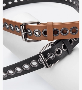 Detail of punk style leather belts with metal eyelets and gunmetal buckles on white stands