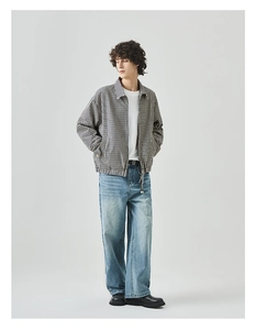 Detail van een zwart-wit geruit jack met ritssluiting, wit T-shirt en blauwe jeans