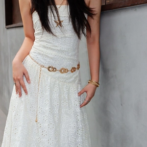 Close-up of golden metal waist chain with circular link design on white lace dress