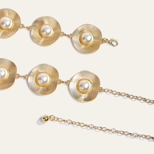 Detailed close-up of golden metal chain belt with sunburst discs and pearl inlays