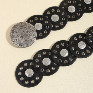 Detalle de cinturón bohemio con círculos de cuero negro y discos de metal plateado martillado
