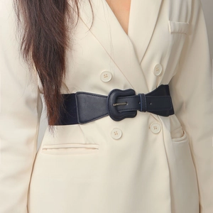 Detail of a wide elastic waist belt with faux leather buckle on a beige blazer