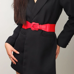 Detail of red elastic waist belt with textured buckle on a black blazer jacket