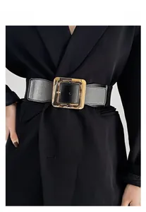 Détail de la grande boucle carrée dorée sur une large ceinture noire en cuir synthétique