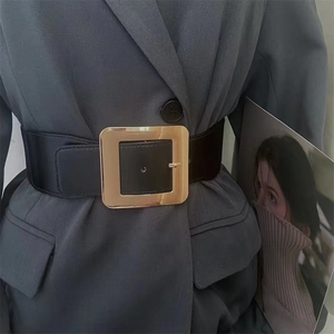 Détail d'une large ceinture noire en similicuir avec boucle dorée carrée sur blazer