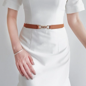 Close-up of slim brown leather belt with gold metal hook buckle on a white dress