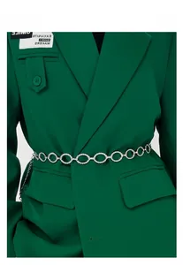 Détail d'une chaîne de taille en métal argenté avec gland sur un blazer vert foncé