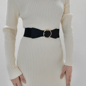 Detail of a black elastic waist belt with a large gold round buckle on a striped dress
