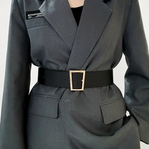 Gros plan sur une large ceinture noire en similicuir avec boucle trapèze dorée sur un blazer