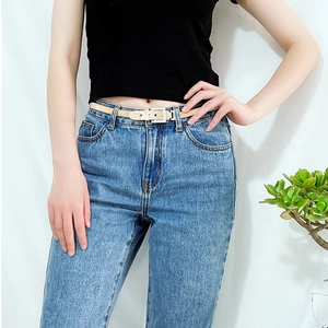 Dettaglio di una cintura beige sottile con fibbia rettangolare in metallo sui jeans
