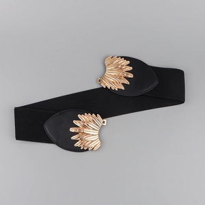 Detailed macro view of the golden wing-shaped buckle on a black elastic waist belt