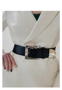 Detail of a wide black elastic waist belt with large silver square metal buckle and tip