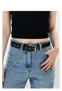 Dettaglio della cintura in PU nero con occhielli argentati e catene sui jeans