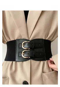 Detail of black wide elastic waist belt with double gold buckles on a beige blazer dress
