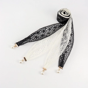 Detail of lace ribbons with floral embroidery and white pearl pendants on golden clips