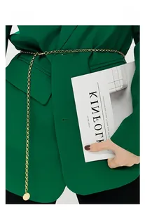 Détail d'une fine ceinture chaîne dorée à anneaux sur un blazer vert avec pendentif