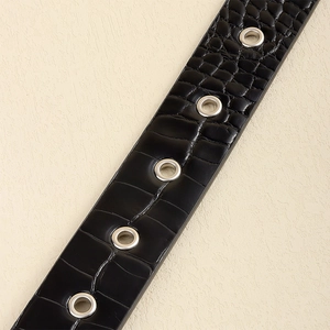 Dettaglio cintura nera in finta pelle di coccodrillo con occhielli metallici color argento