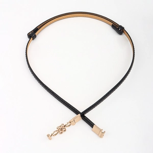 Detail of slim black PU leather belt with decorative gold knot buckle and neat stitching