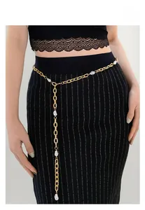 Detail of elegant gold metal waist chain with pearls on a black dress and model