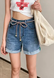 Detail of light blue denim shorts featuring a thin pink belt with pearl charms