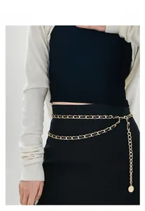 Détail d'une ceinture chaîne dorée multicouche avec cuir tressé noir et pendentif