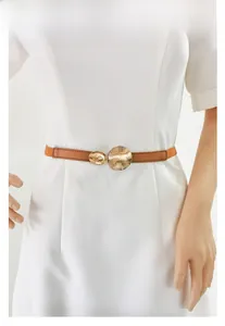 Détail d'une ceinture marron texturée avec boucle dorée élégante sur une robe blanche