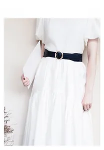 Styling detail of a black wide belt with gold round buckle on a white dress