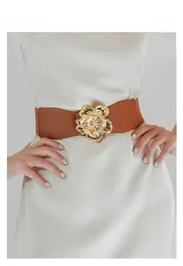Detail of a brown elastic waist belt featuring a gold floral buckle on a cream dress